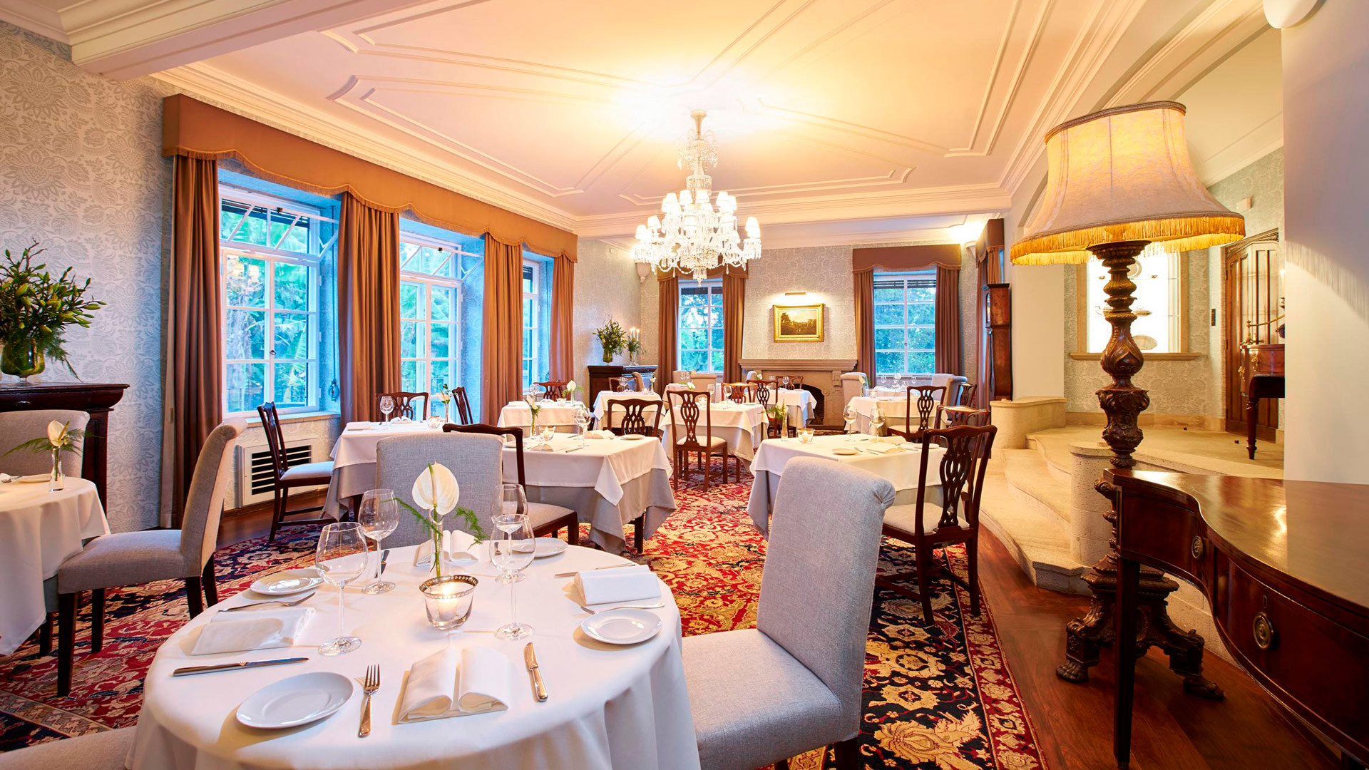 Raum dekoriert mit gedeckten Tischen, Stühlen und zentraler Lampe.