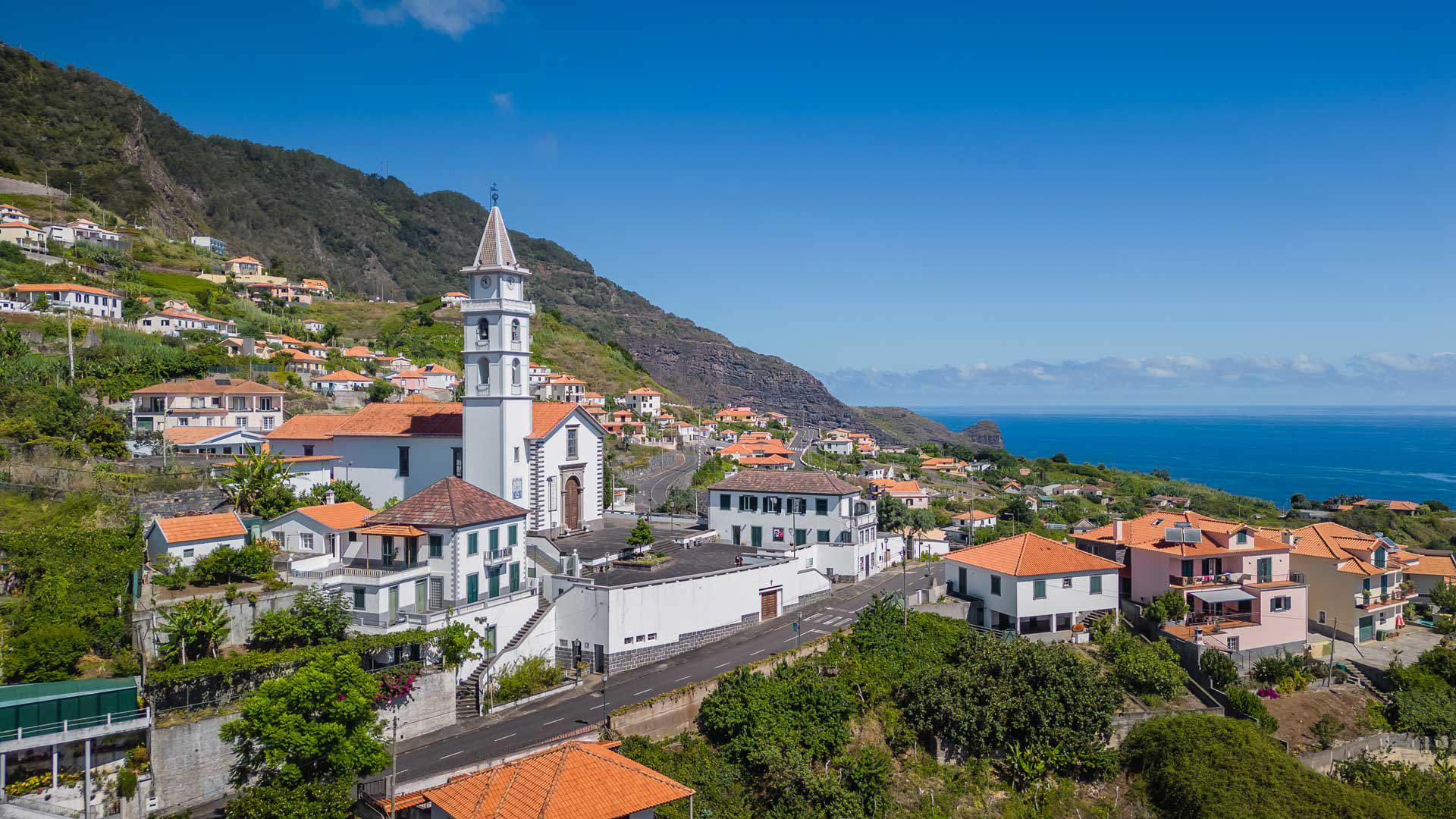 Kirche und Häuser umgeben von Natur in Madeiras Landschaft.