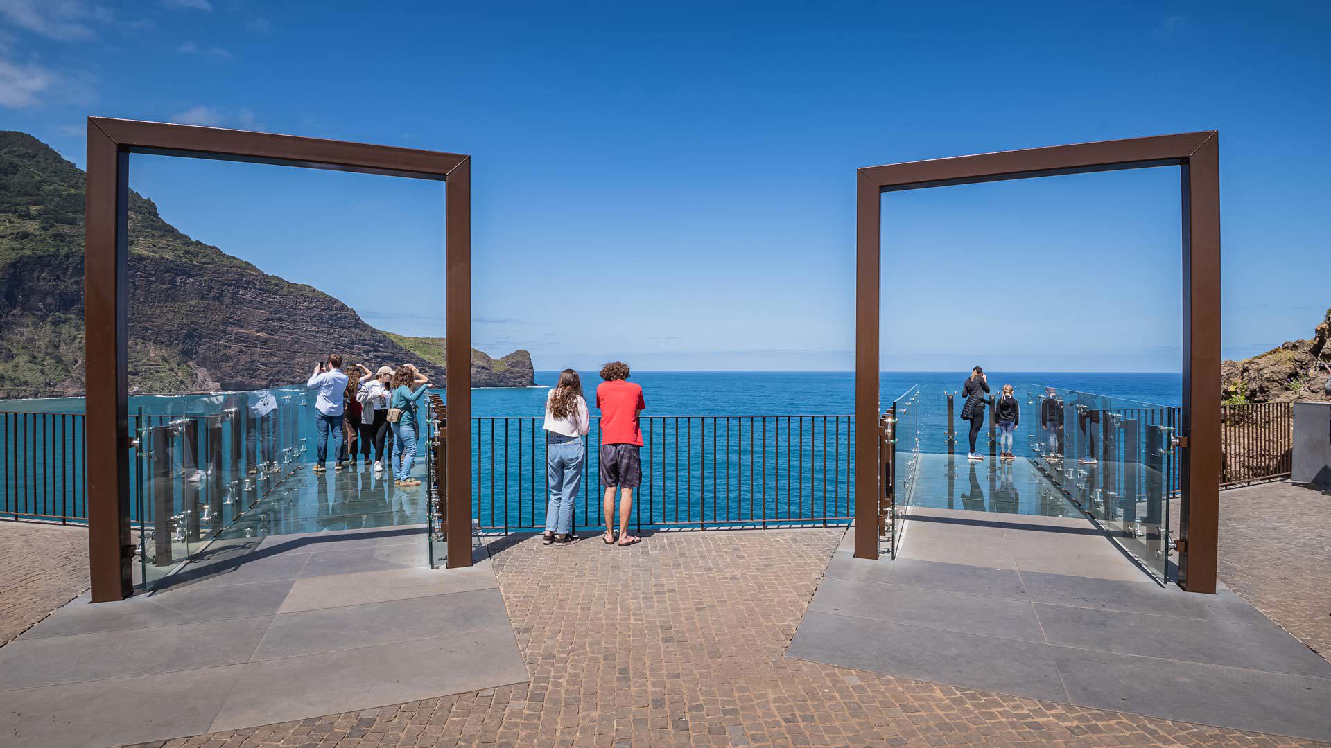 Personas en un mirador de vidrio con vistas al mar y montaña en Madeira.