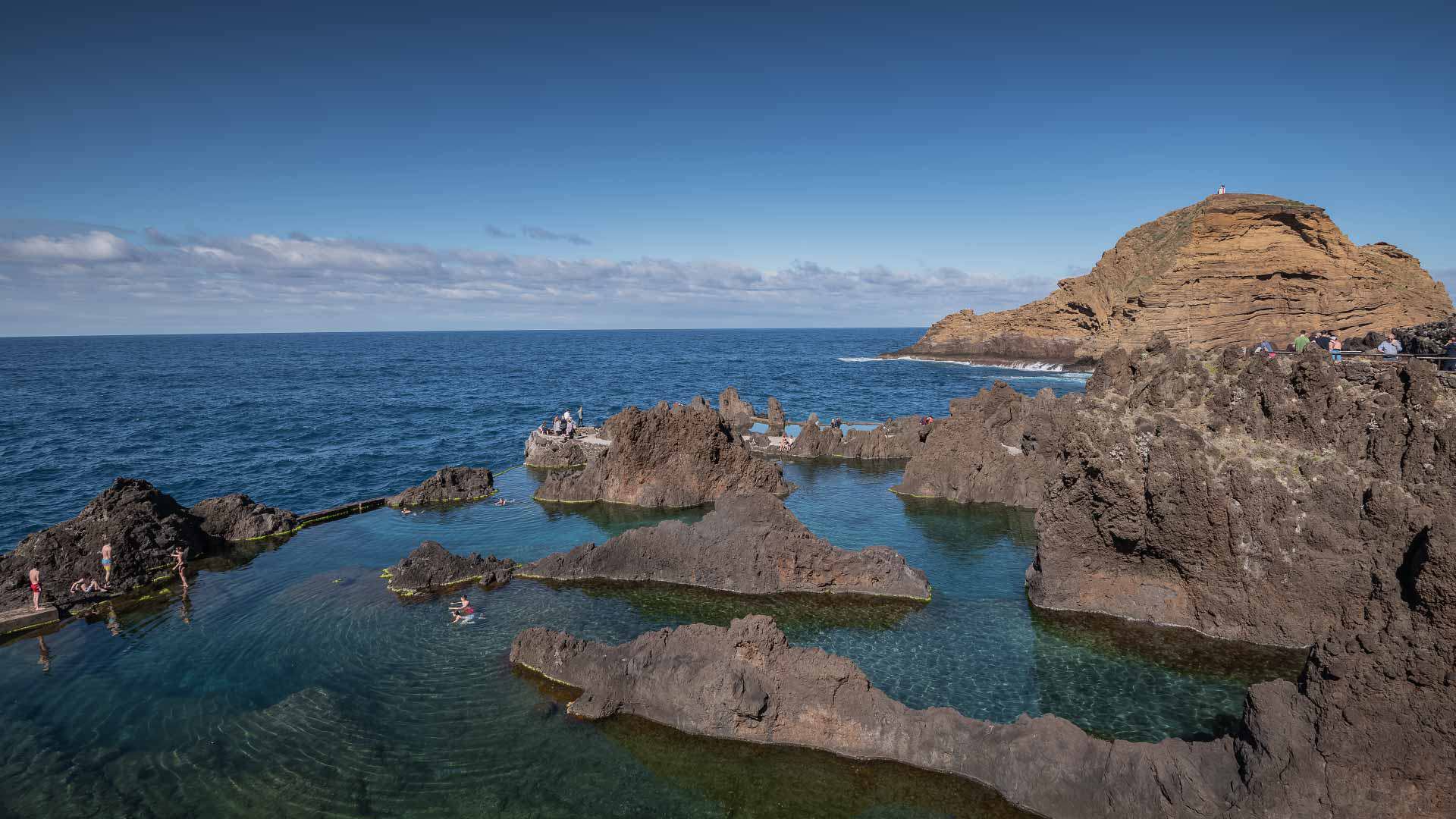 Piscina natural entre rochas junto ao mar, com uma grande rocha em destaque.