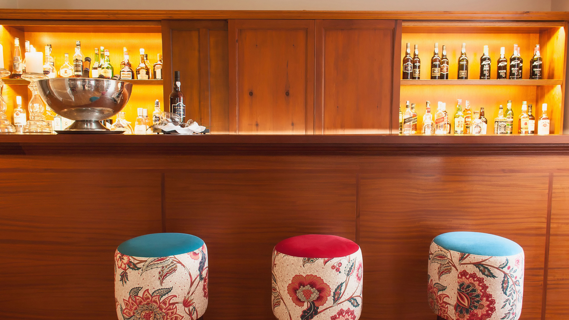 Mostrador con bebidas y tres taburetes pequeños.