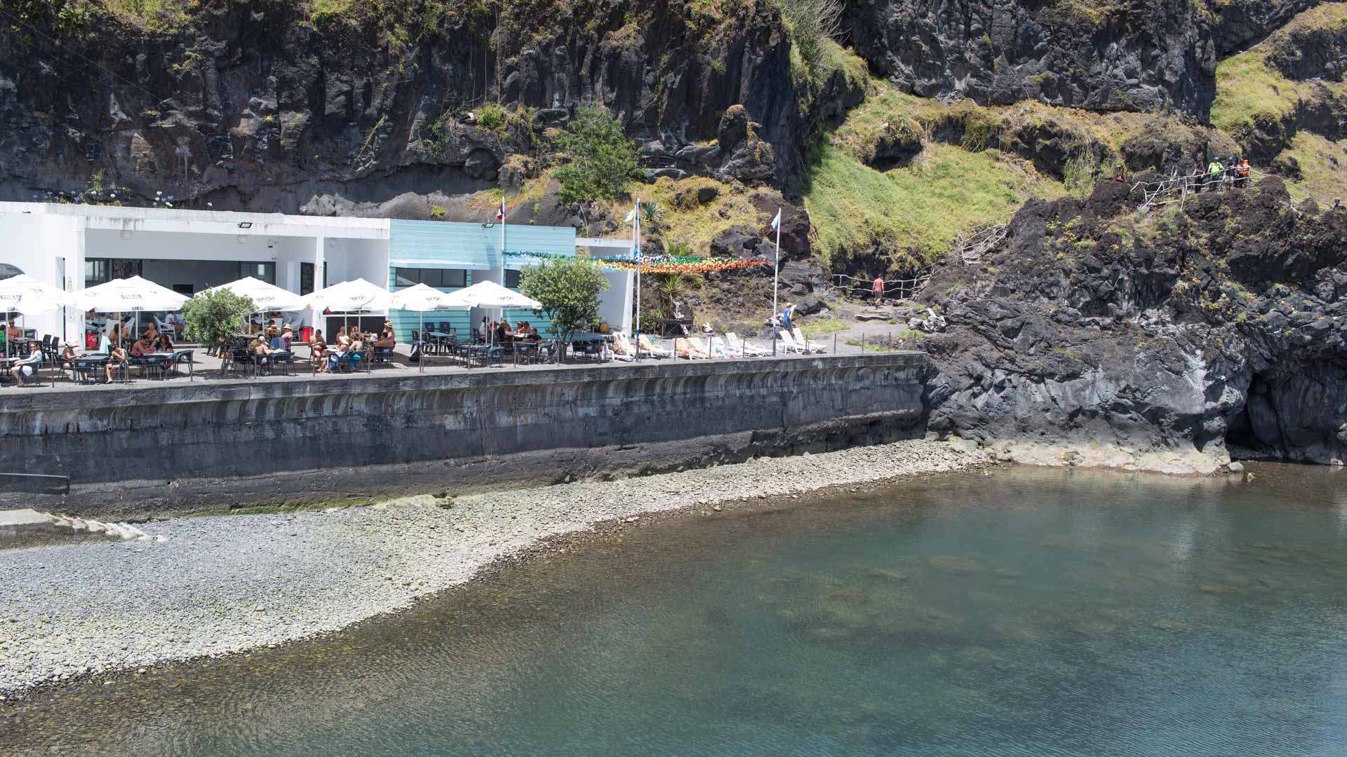 Terrasse am Meer mit weißen Sonnenschirmen und Bergen im Hintergrund auf Madeira.