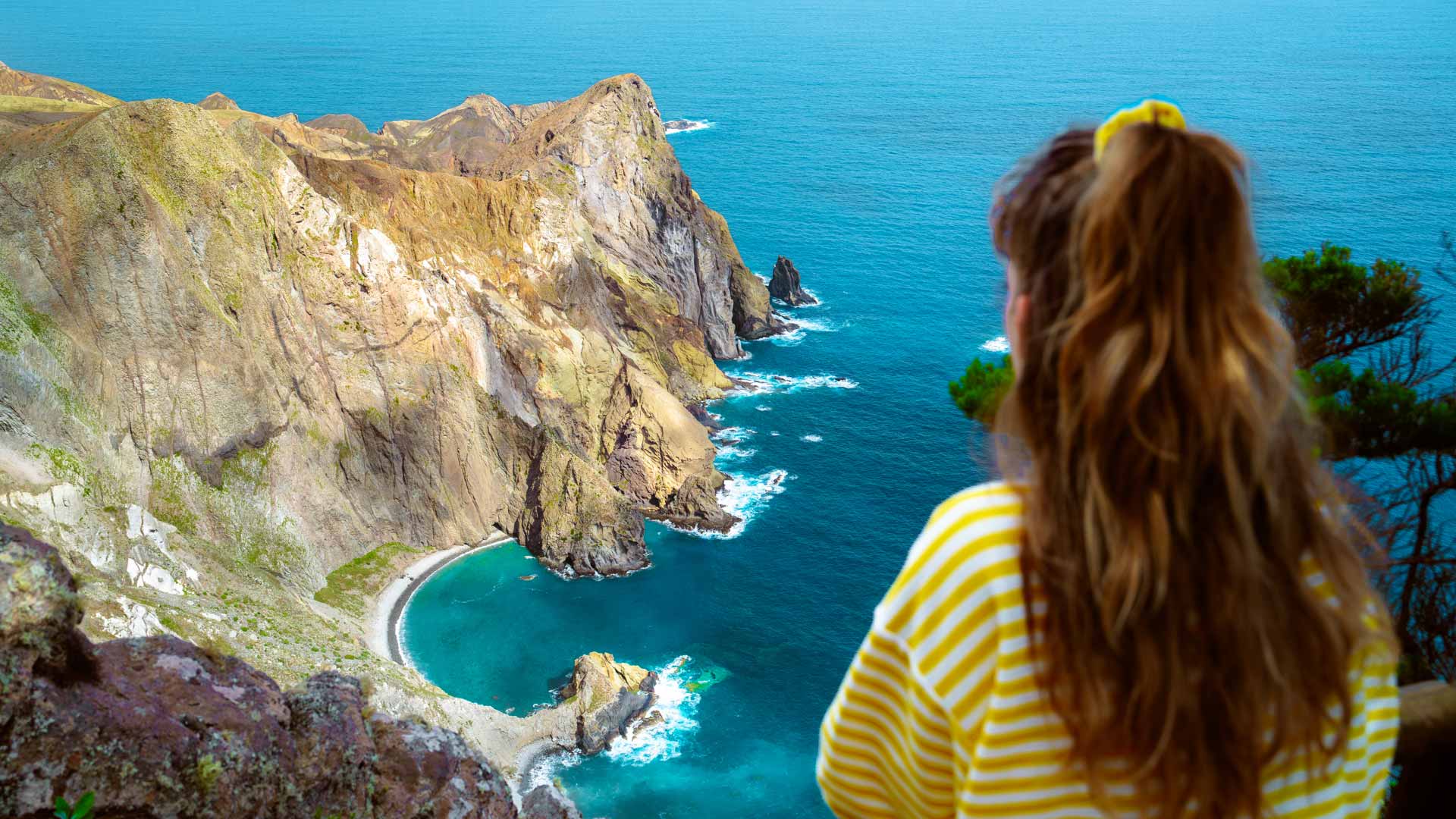 Femme en chemise jaune à rayures blanches, avec montagne et mer en arrière-plan.