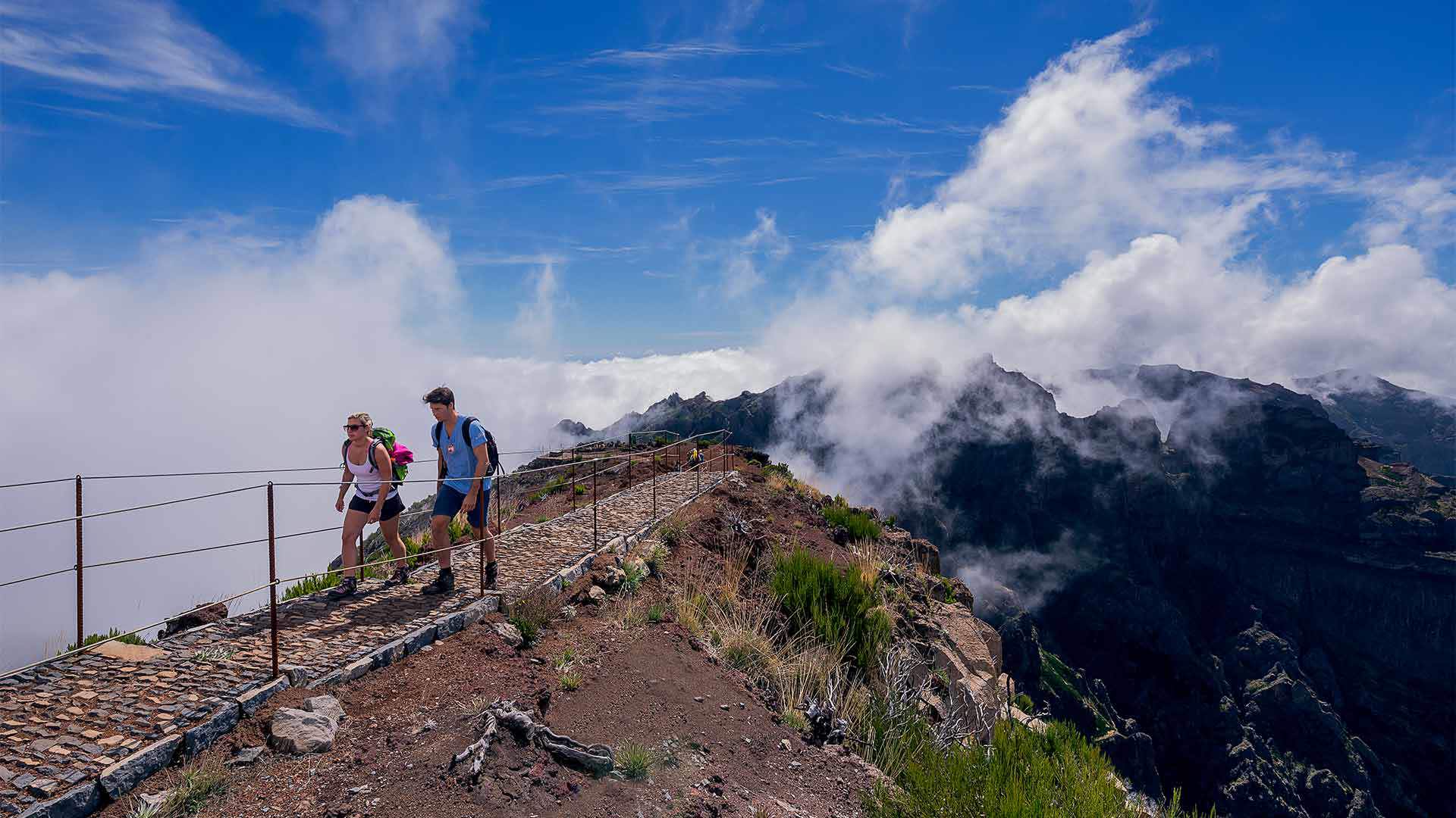 Two people walking on a mountain trail with clouds in Madeira.