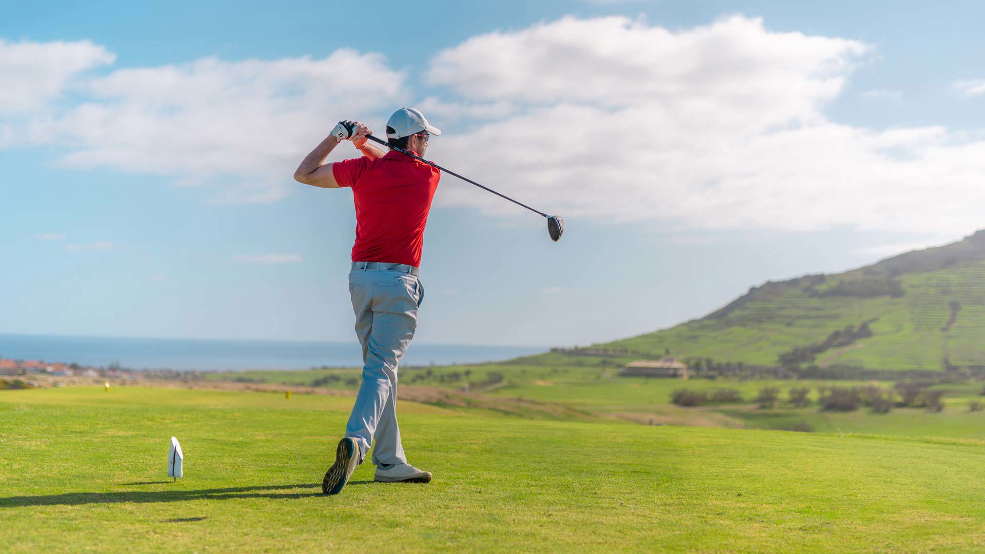 Man playing golf on a wide, green course.