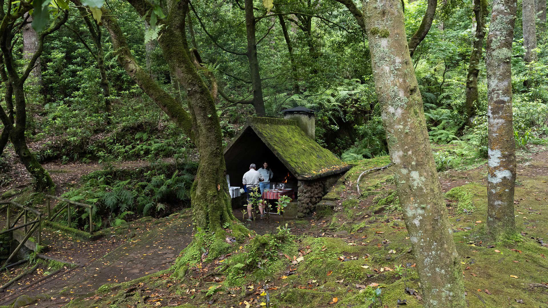Espetada serviert in den Bergen, mit Unterstand, Vegetation und Menschen drumherum.