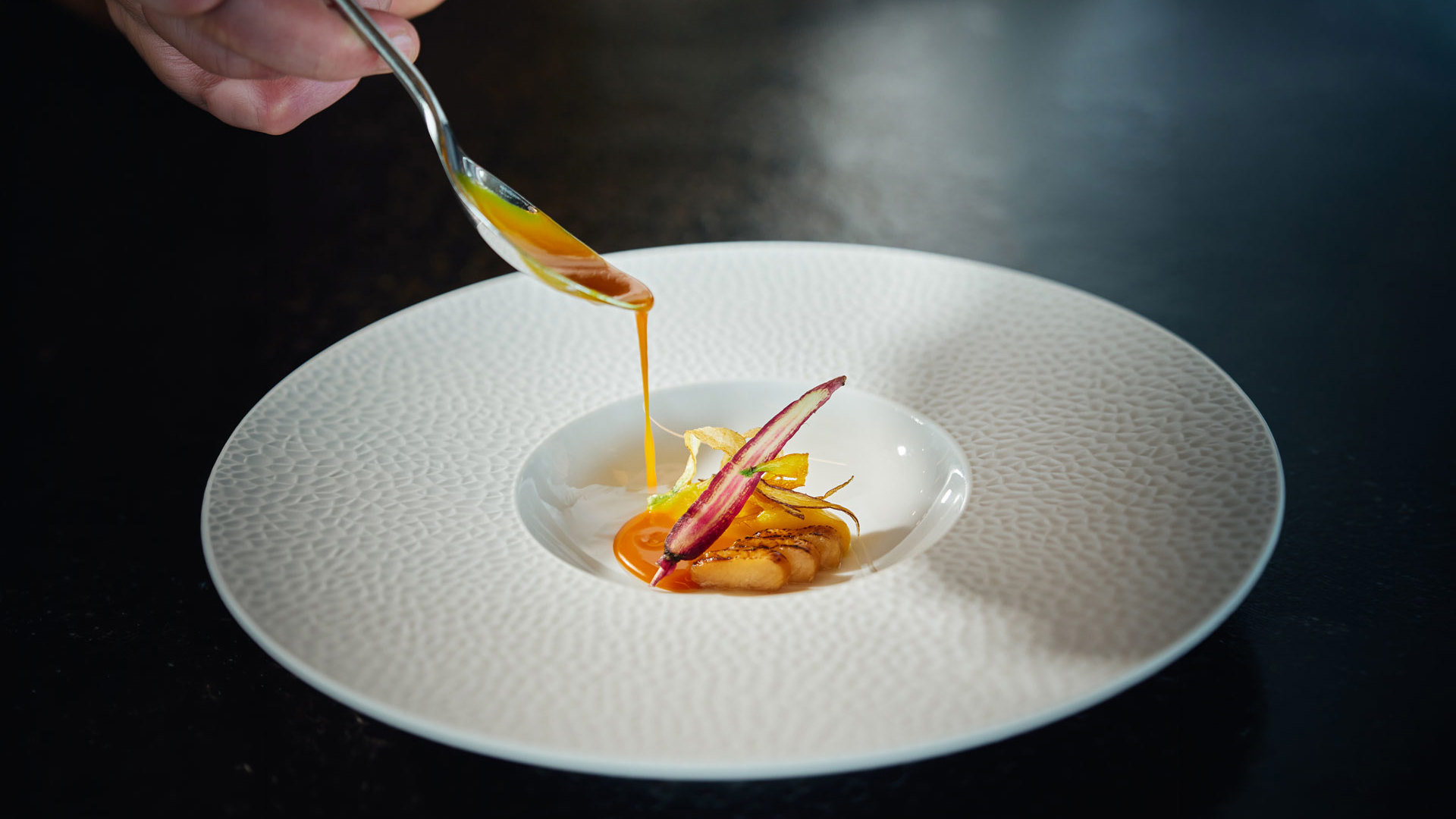 Hand serviert ein Dessert mit einem Löffel auf einem Teller, inspiriert von der Gastronomie der Insel Madeira.