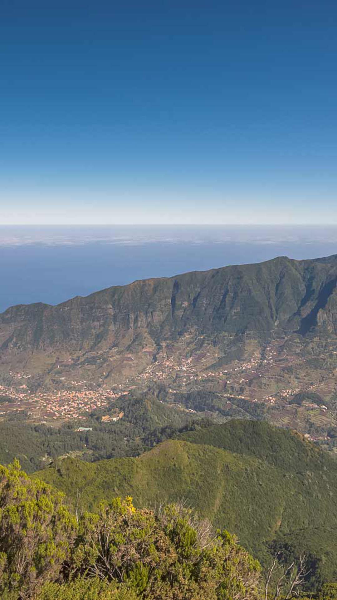 Vallée verte avec maisons, mer en fond et nature environnante.