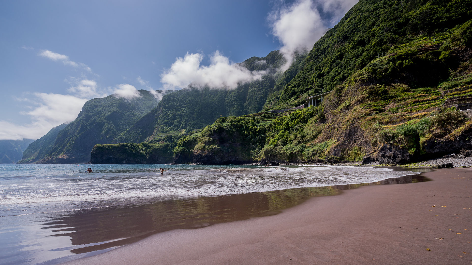 Praia de areia preta com mar e montanhas ao fundo na Madeira.