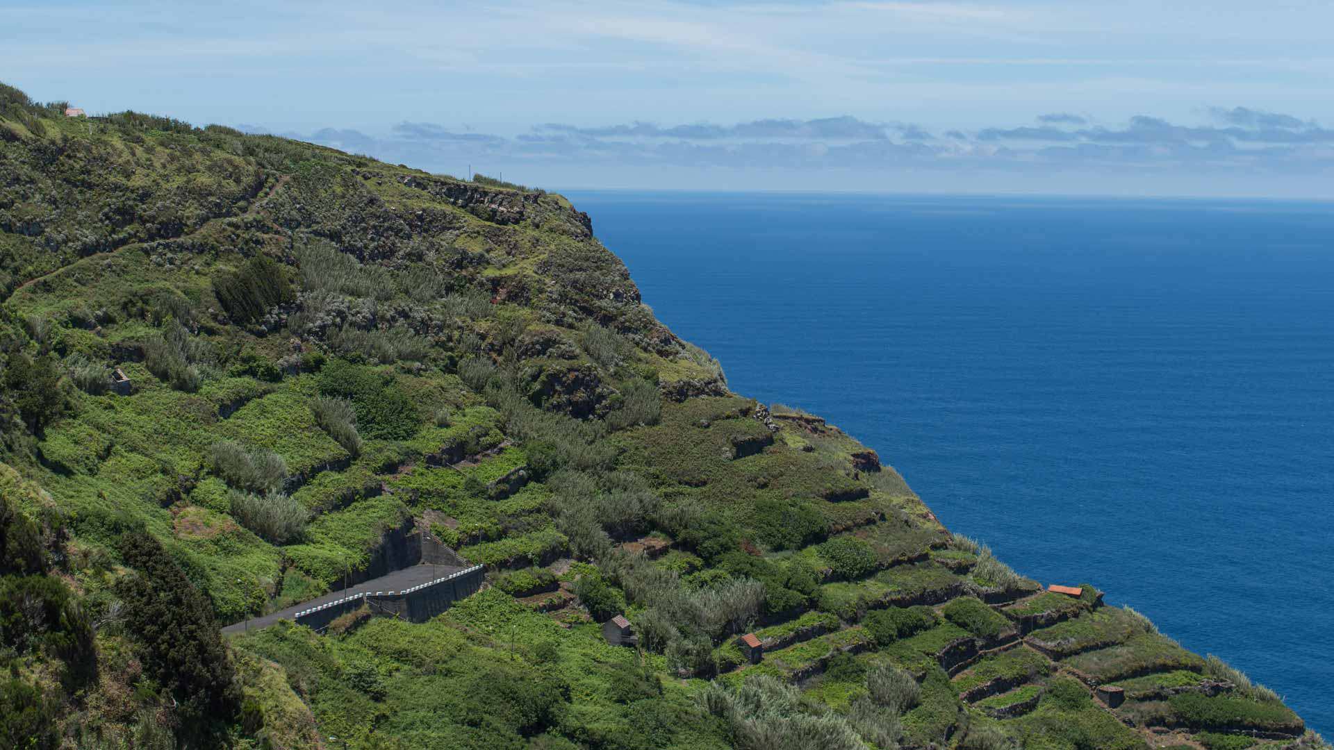 Encosta verde com mar azul ao fundo em paisagem natural.