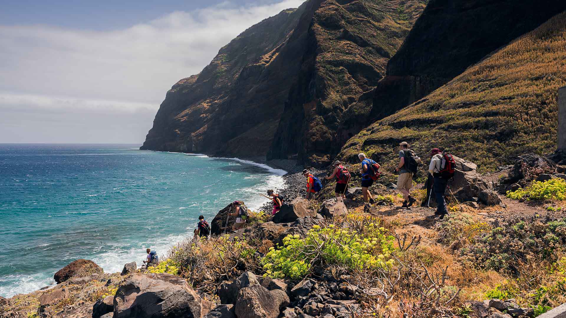 Caminhantes a descer encosta com montanha e mar ao fundo na Madeira.