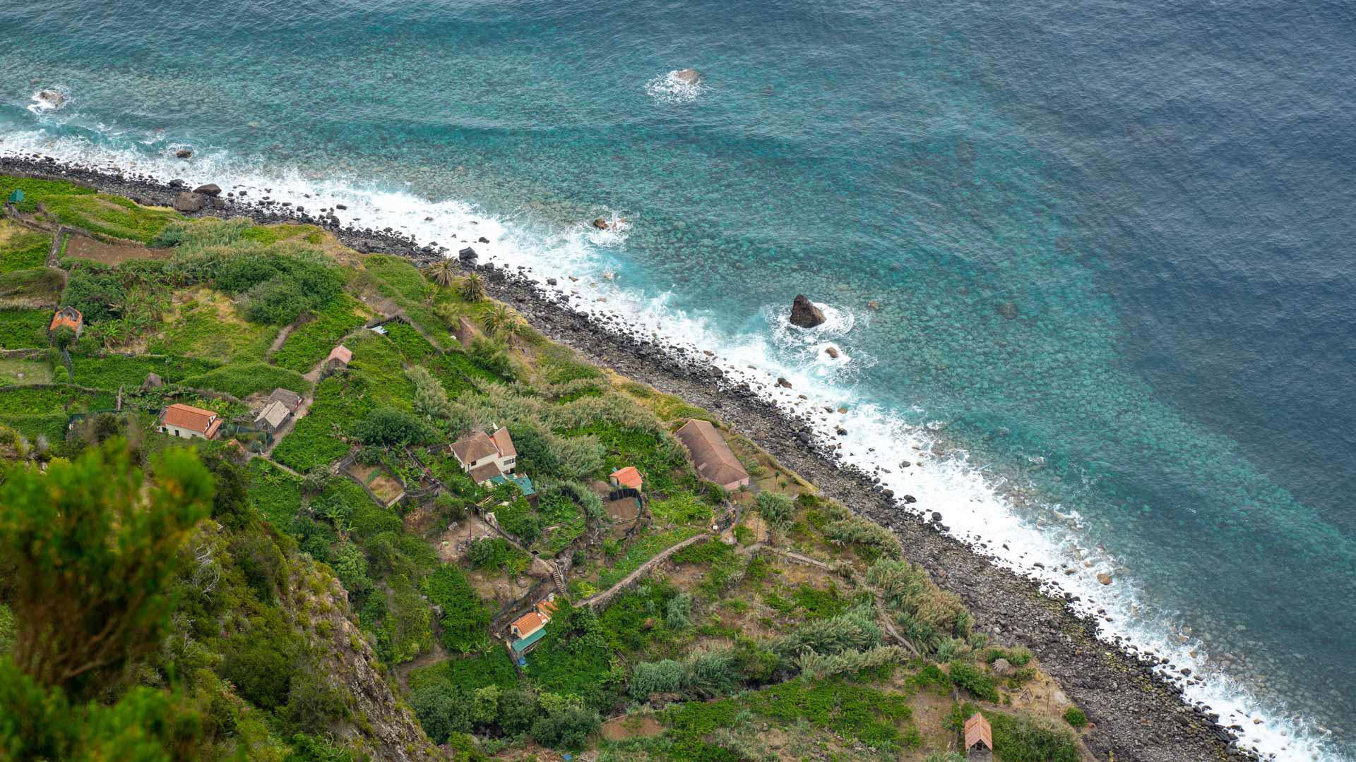 Terrains verts avec maisons près de la plage de galets et la mer.