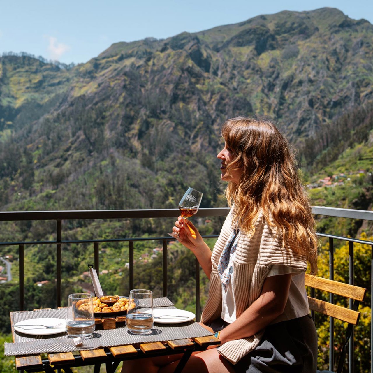 Woman having lunch on a terrace in Curral das Freiras, surrounded by mountains and vegetation.