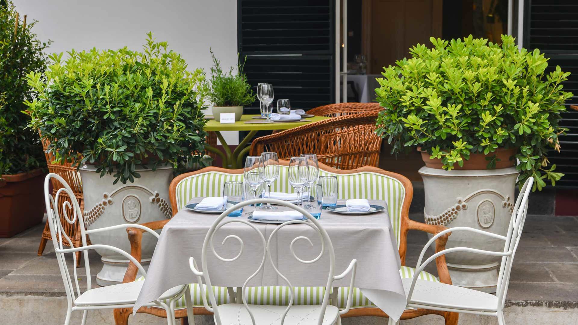 Gedeckte Tische im Außenbereich eines Restaurants, umgeben von Pflanzen.