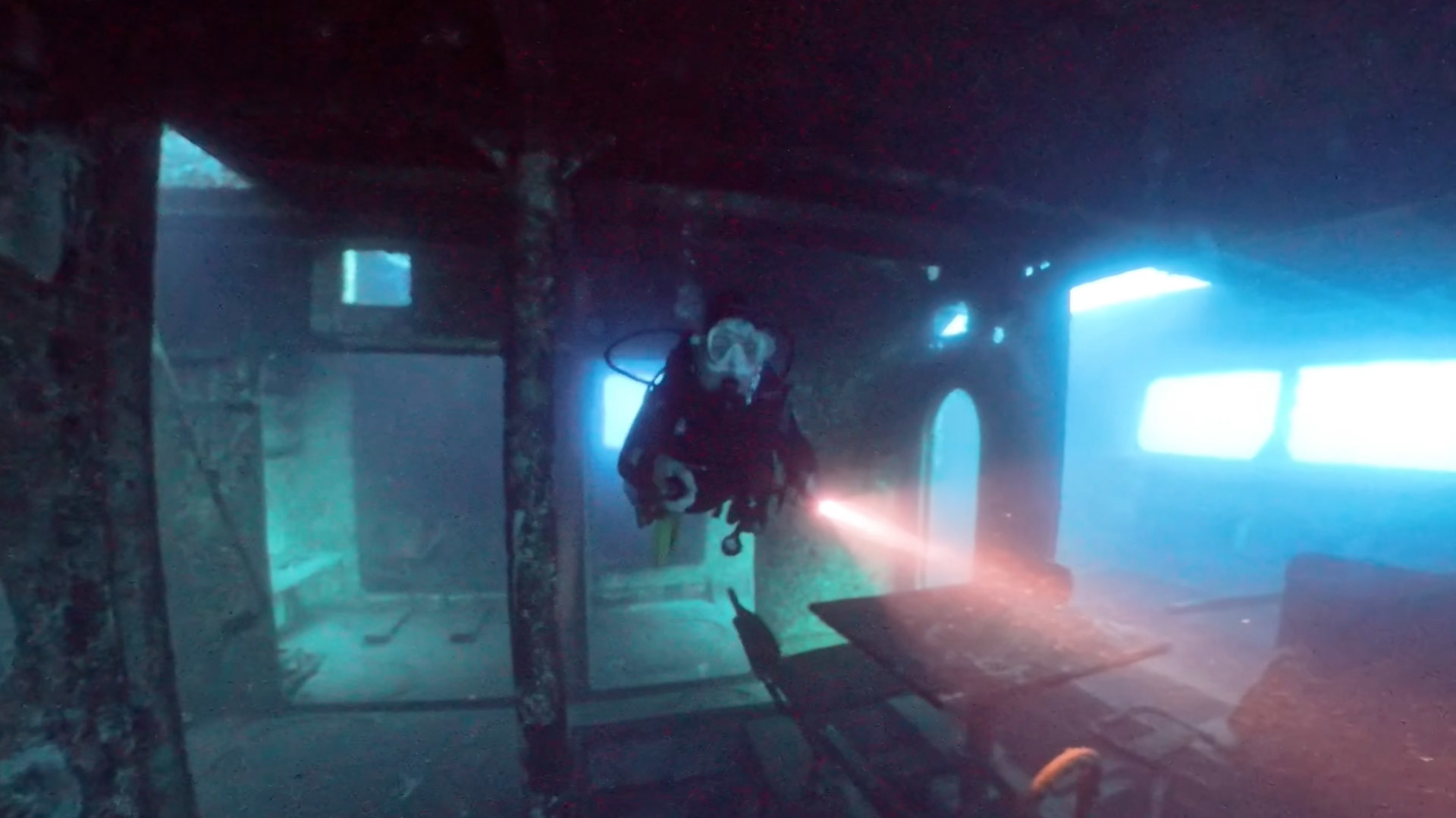 Mulher a mergulhar junto a um navio afundado, equipada com equipamento de mergulho.