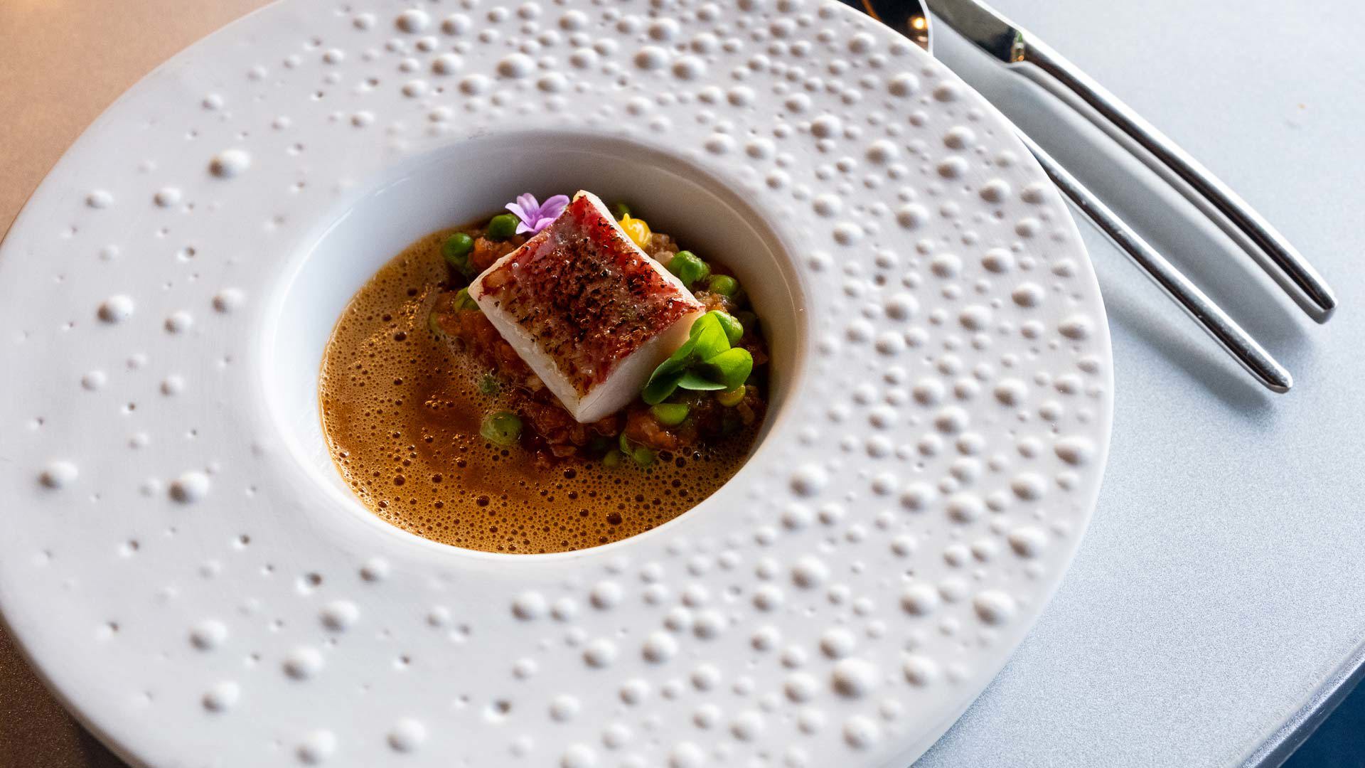 Runde weiße Platte mit Gourmet-Anrichtung, dekoriert mit Blumen.