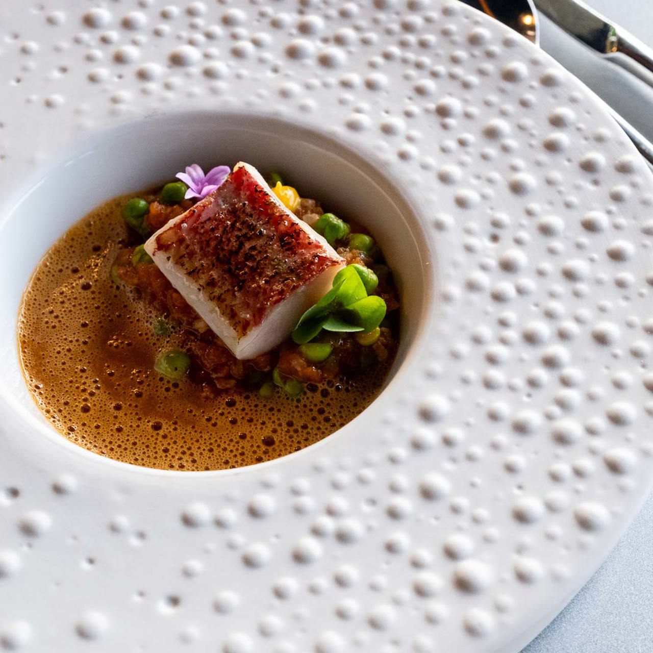 Runde weiße Platte mit Gourmet-Anrichtung, dekoriert mit Blumen.