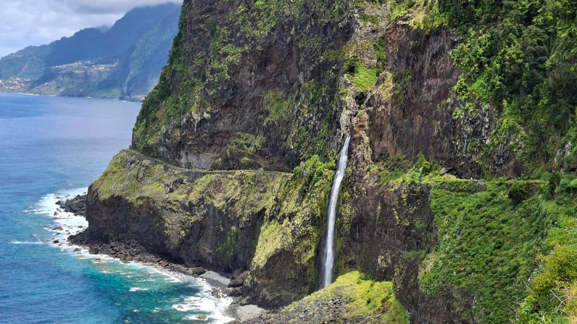 Veu da Noiva waterfall in Madeira, hillside with vegetation and sea in the background.