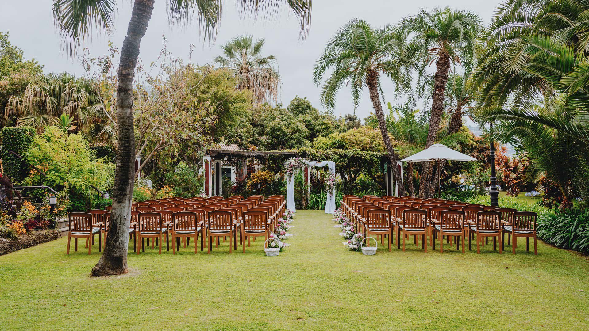 Freiluft-Hochzeitszeremonie mit angeordneten Stühlen und dekoriertem Bogen, umgeben von Natur. 