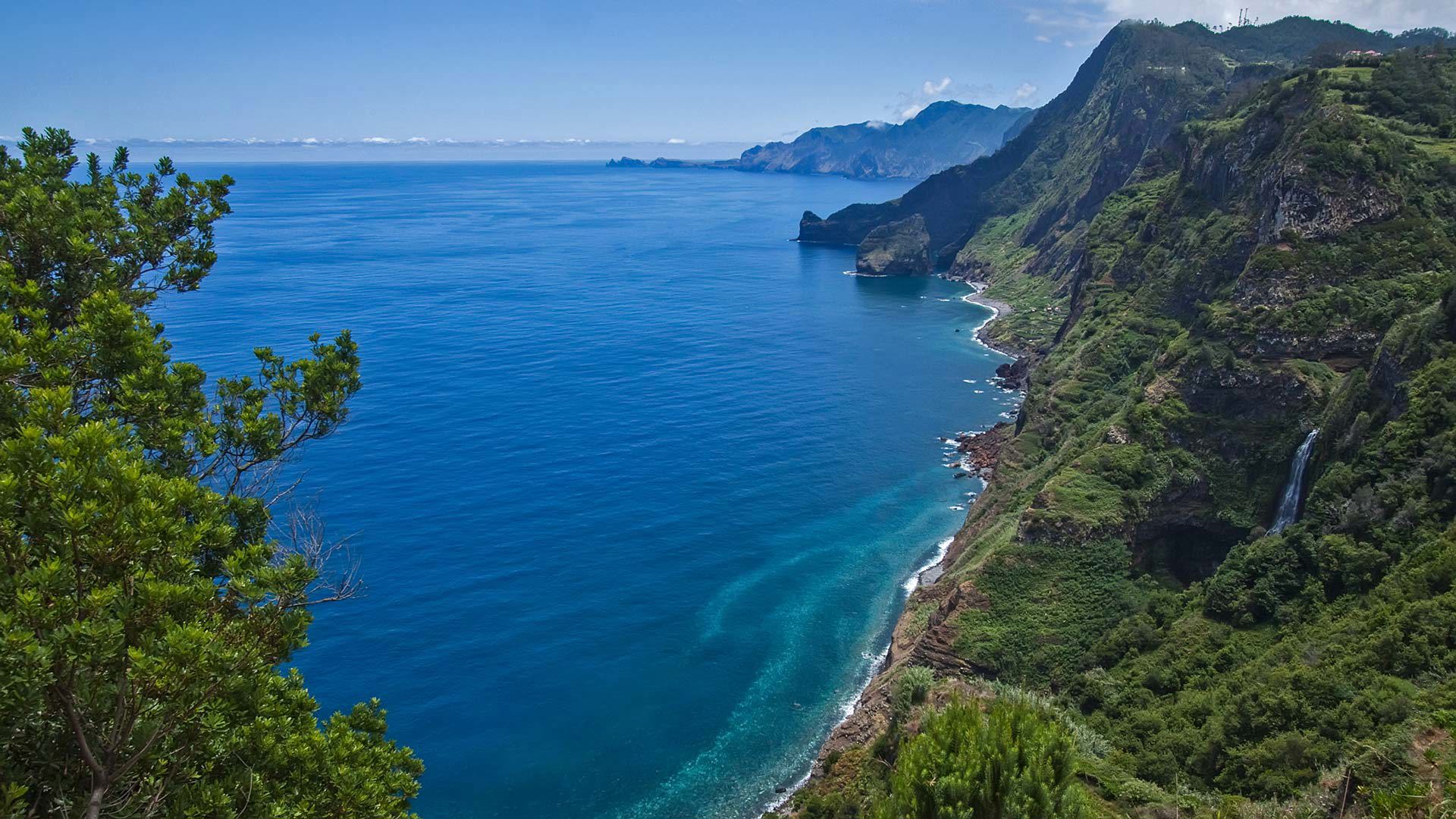 Grüner Hang mit Wasserfall am Meer auf Madeira.