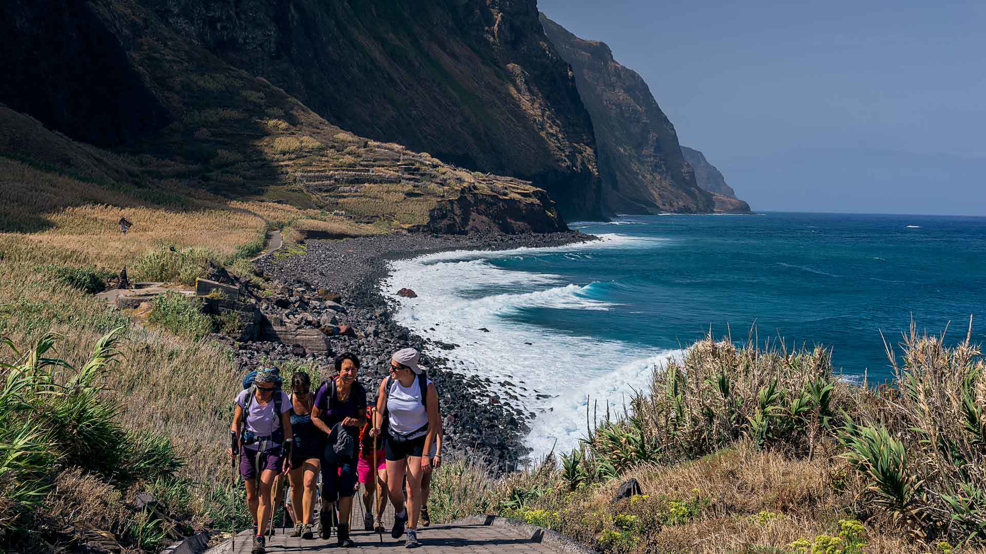 Pessoas a andar perto do mar com montanha ao fundo na Madeira.