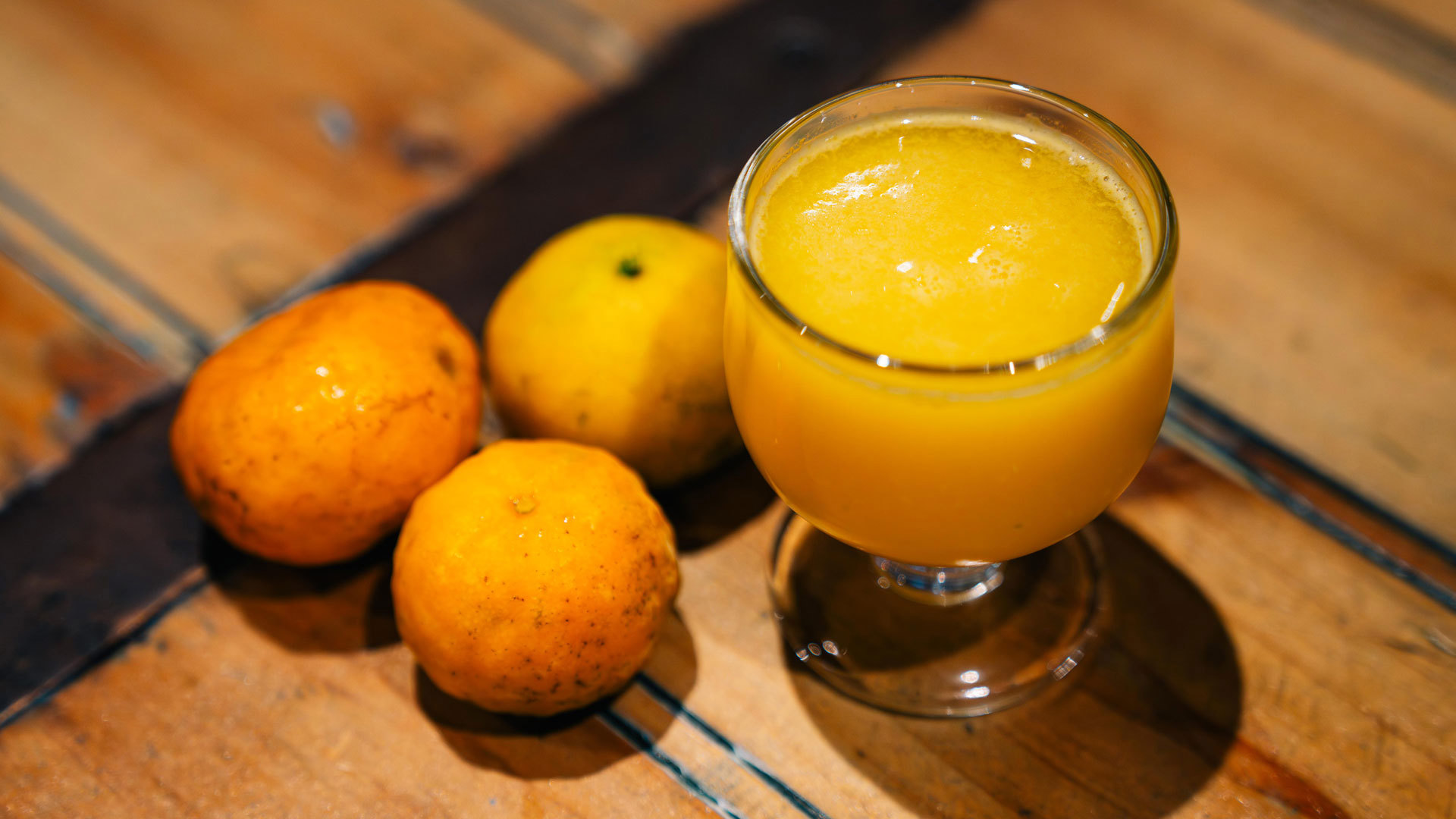 Ein Glas Poncha begleitet von drei Mandarinen auf einer Oberfläche.