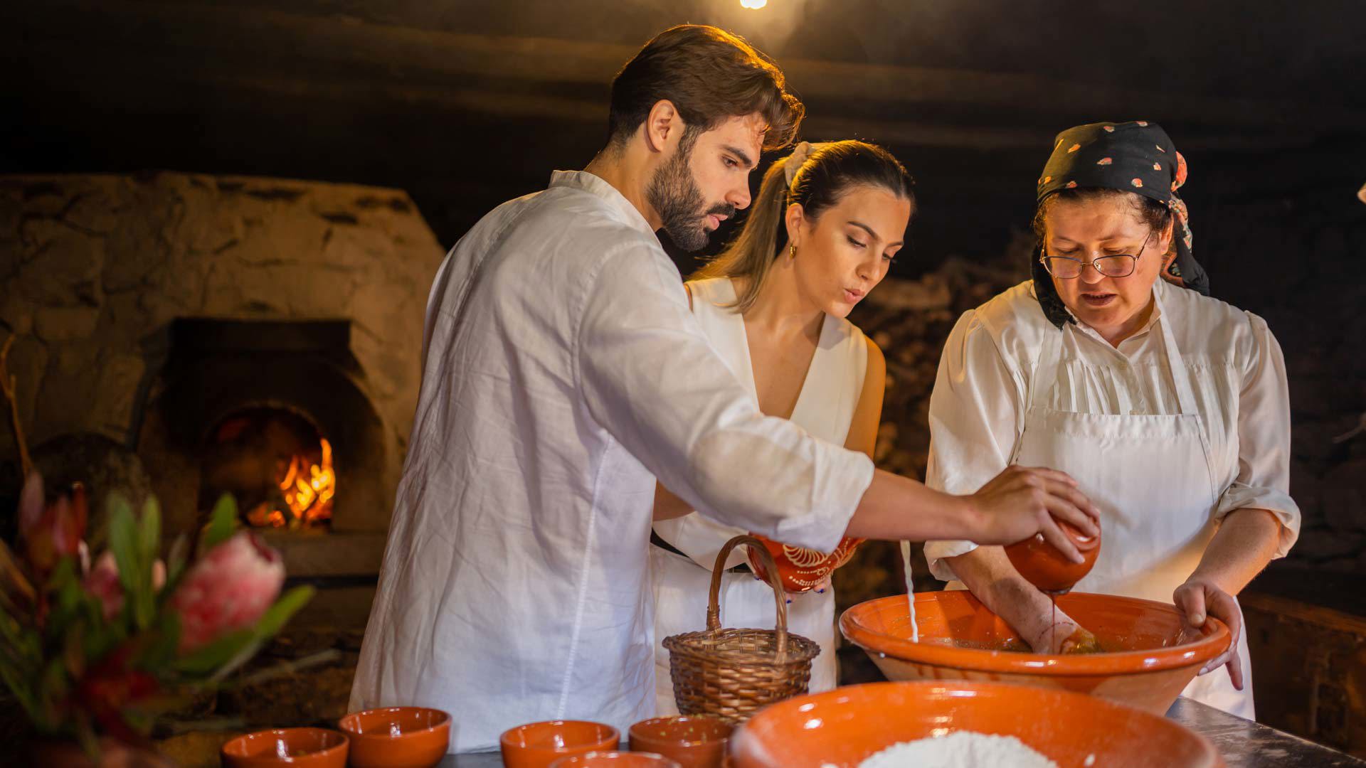 Pareja ayudando a cocinera tradicional con vajillas de barro en Madeira.