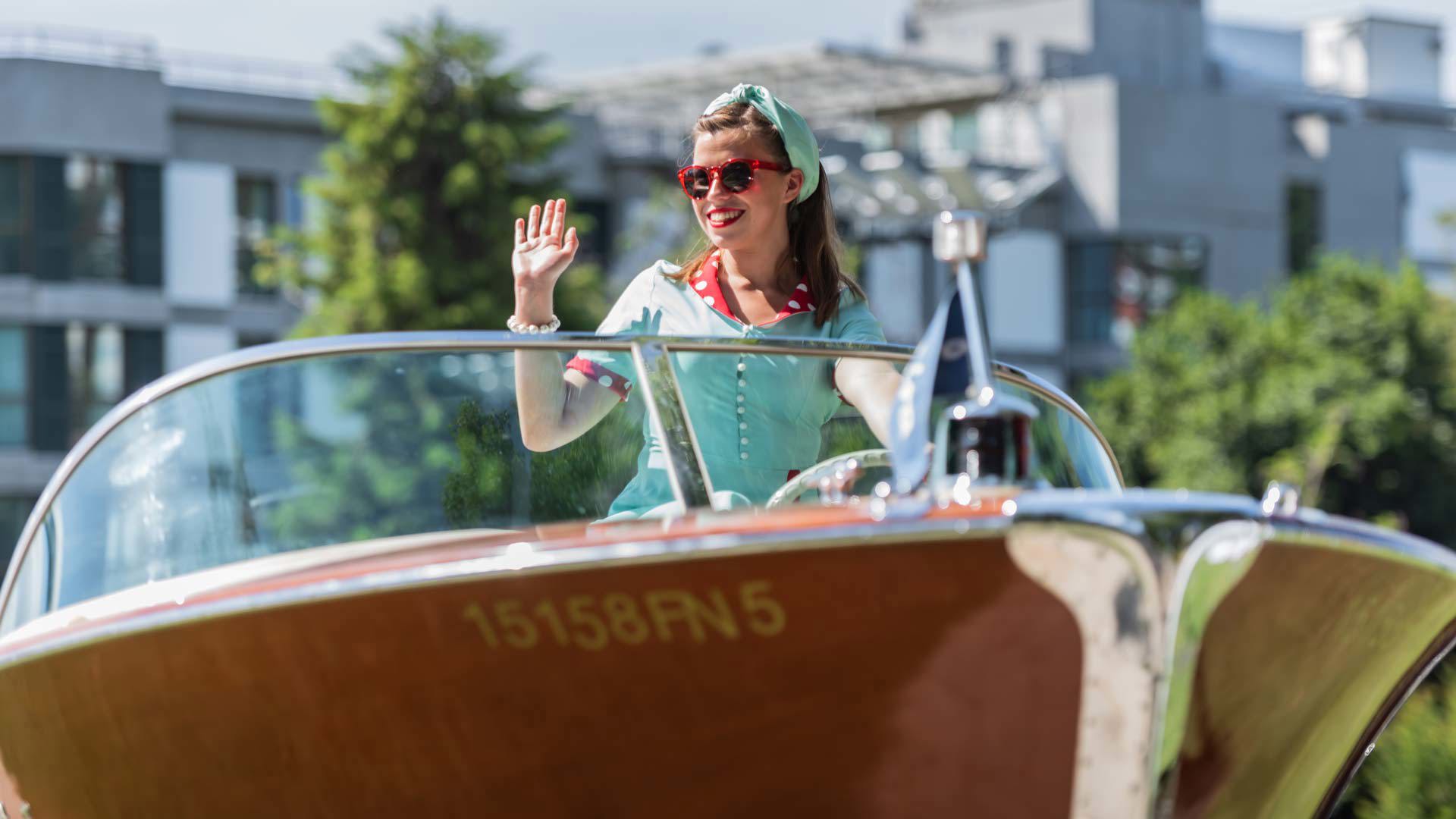 Femme saluant depuis l’intérieur d’un bateau classique exposé.