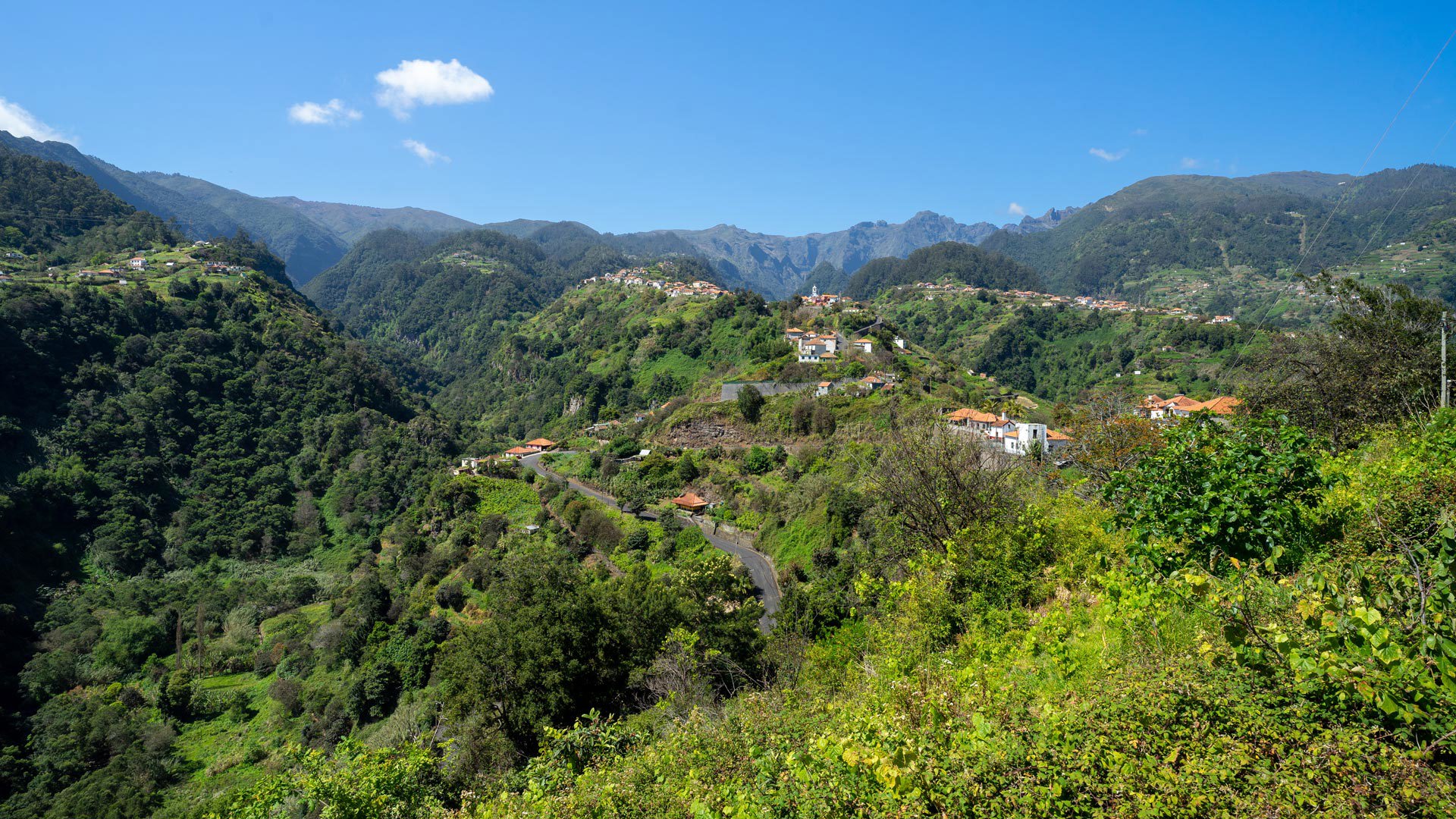 Montanhas verdes com casas sob céu azul na Madeira.