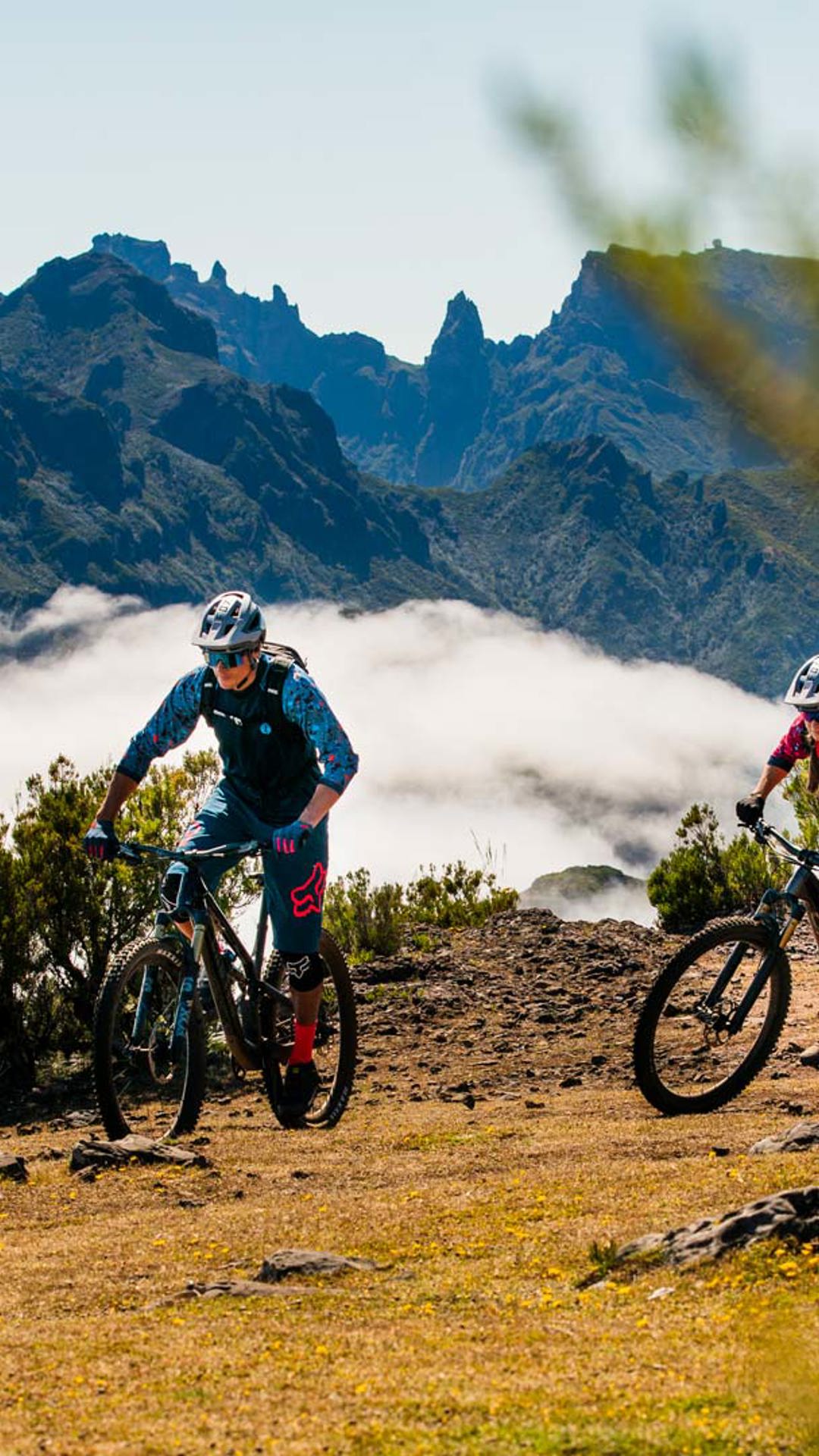 Two cyclists on a mountain trail under a cloudy sky.
