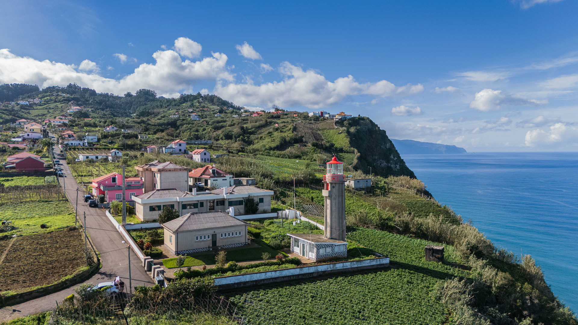 Houses and cultivated land with lighthouse by the sea.