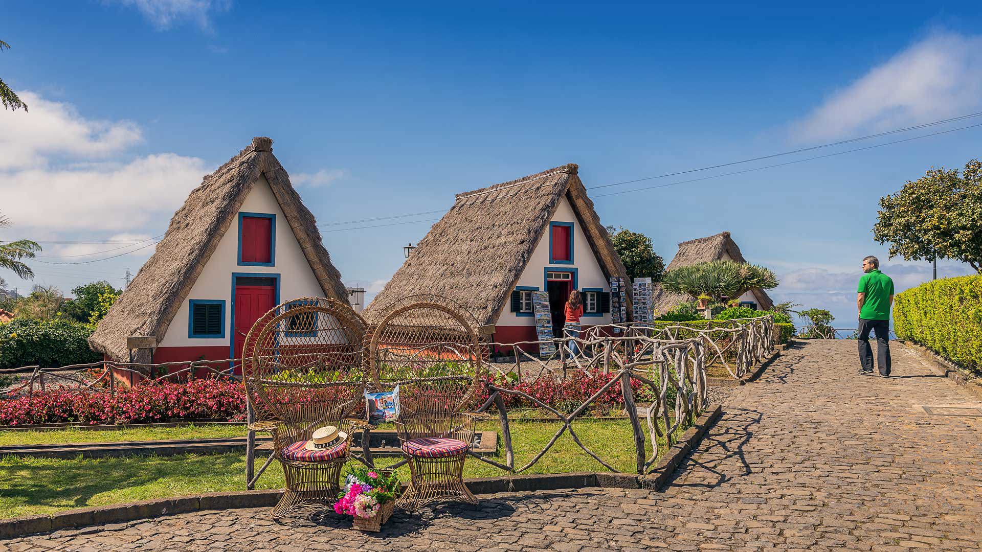 Hombre con camisa verde junto a casa triangular con techo de paja.