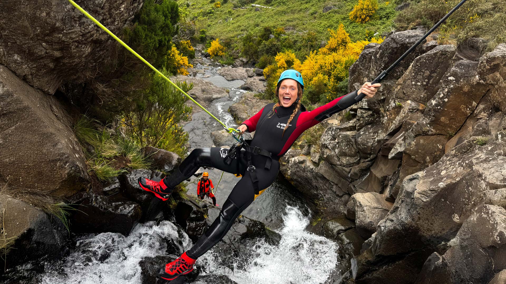 Duas mulheres a praticar canyoning equipadas, junto a uma cascata.