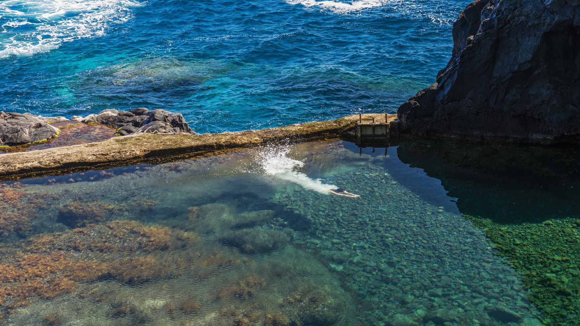 Person schwimmt im Naturpool am Meer auf Madeira.