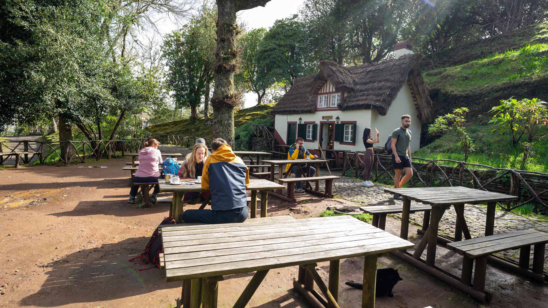 Personas sentadas en mesas de pícnic junto a una casa en la naturaleza en Madeira.