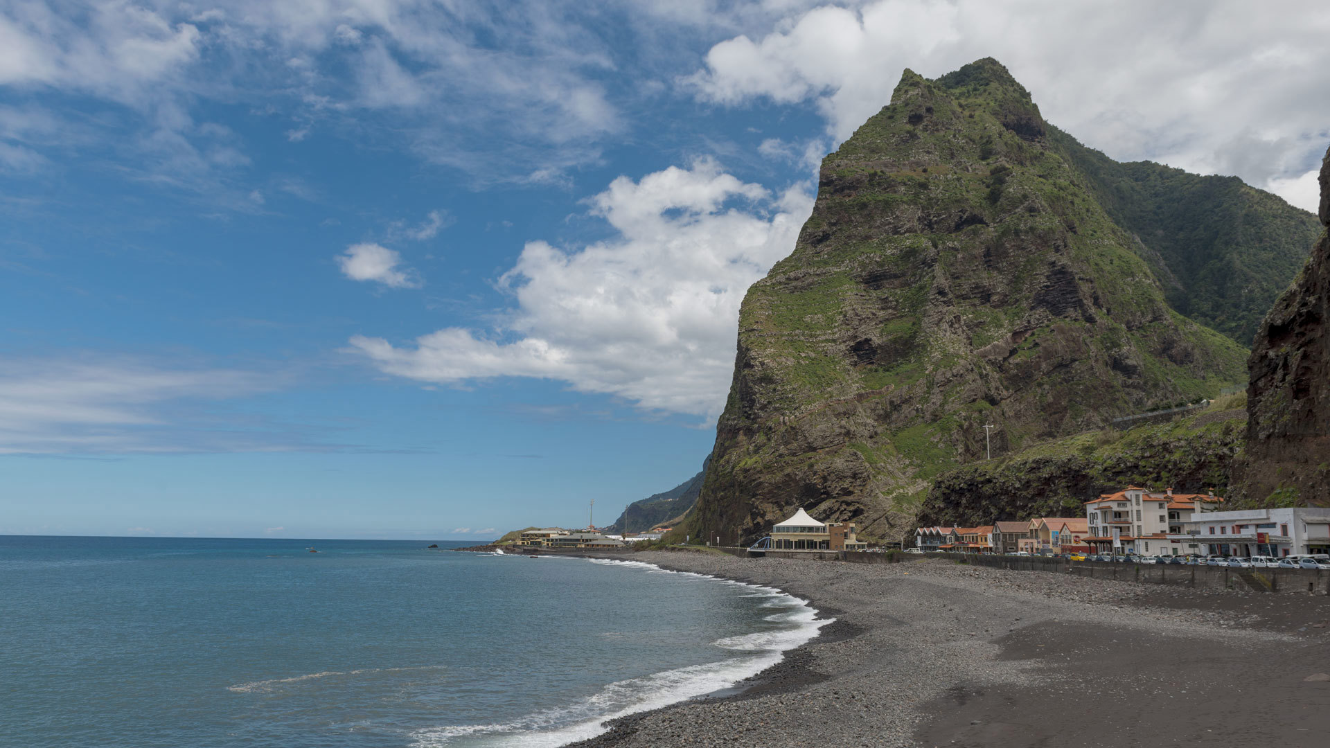 Praia junto à montanha com céu e nuvens na Madeira.