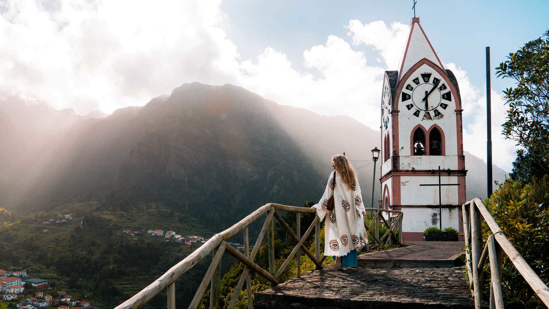 Iglesia rodeada de naturaleza con una mujer disfrutando del paisaje soleado, en la isla de Madeira.