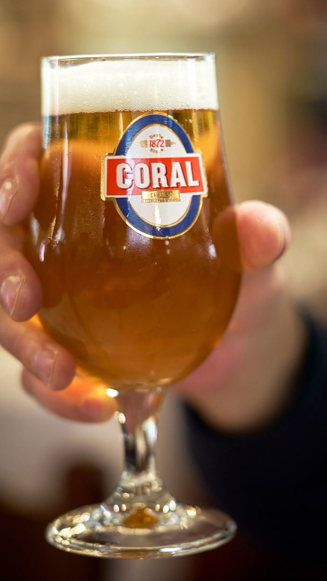 Hand holding a glass of Coral beer on Madeira Island.