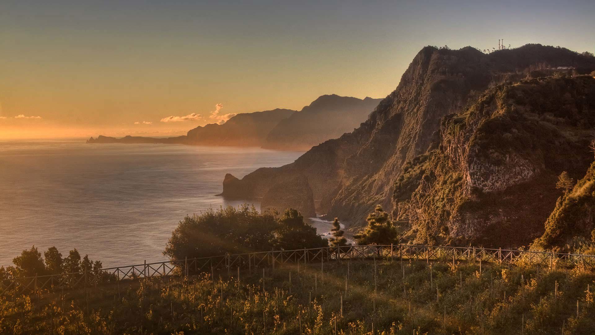Sonnenuntergang über Feldern mit Bergen und Meer auf Madeira.