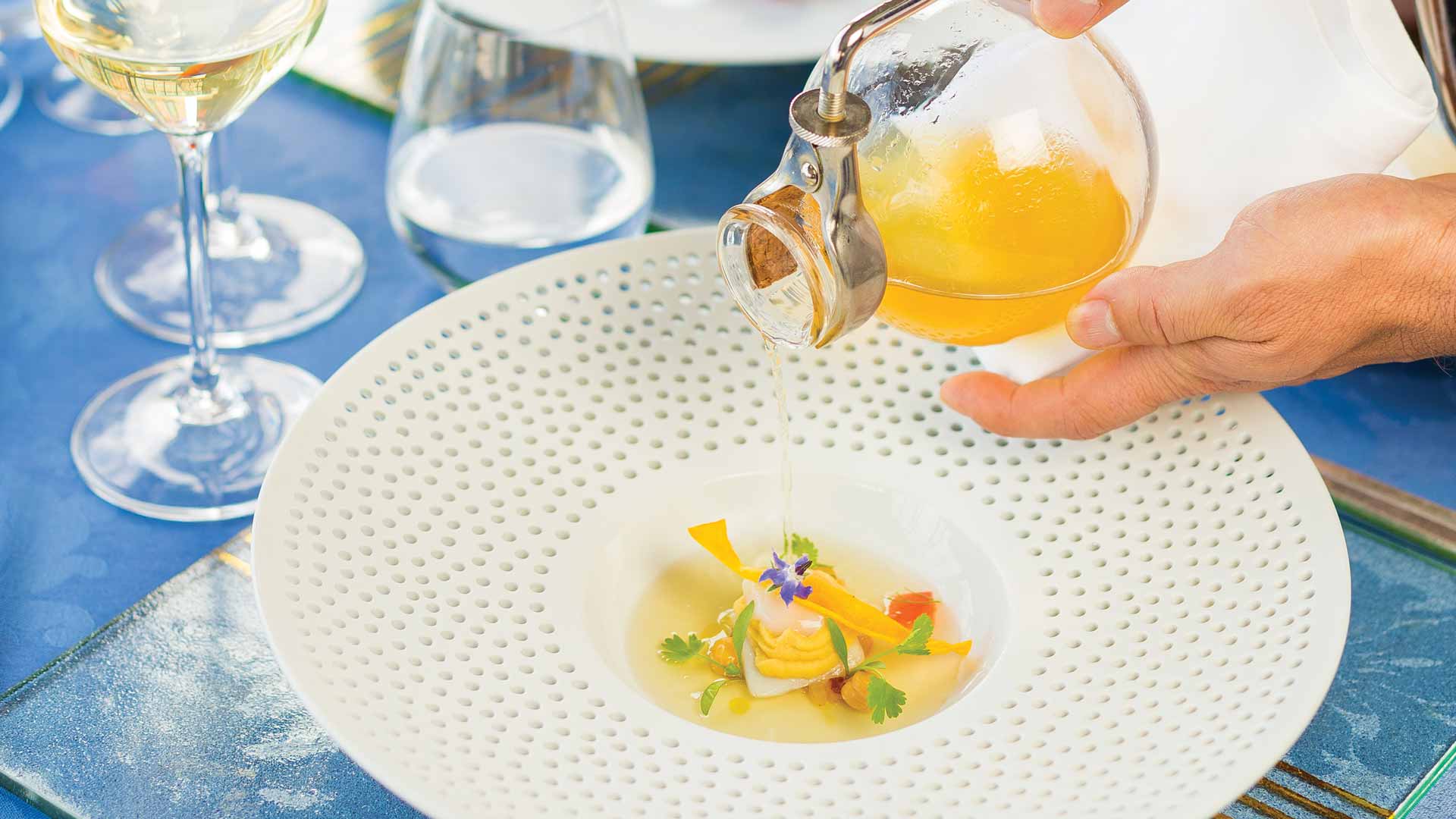 Plato con comida emplatada y copas de vino sobre la mesa, al estilo de gastronomía contemporánea.