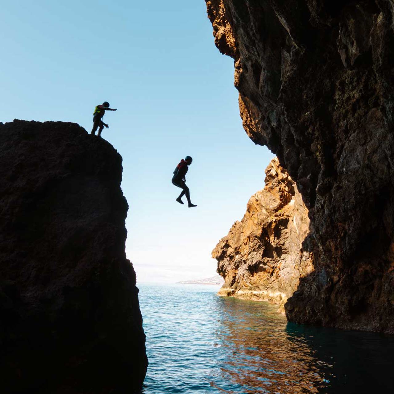 Two people jumping into the sea during a coasteering activity on Madeira Island.