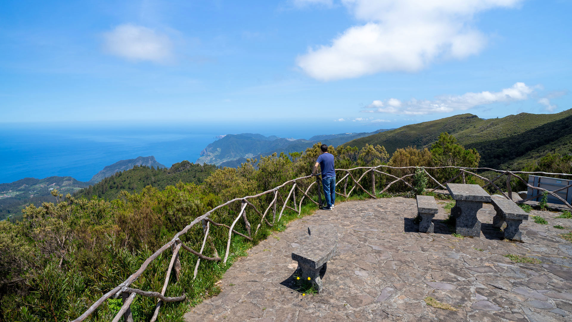 Miradouro com bancos de pedra e vista para montanhas e mar.