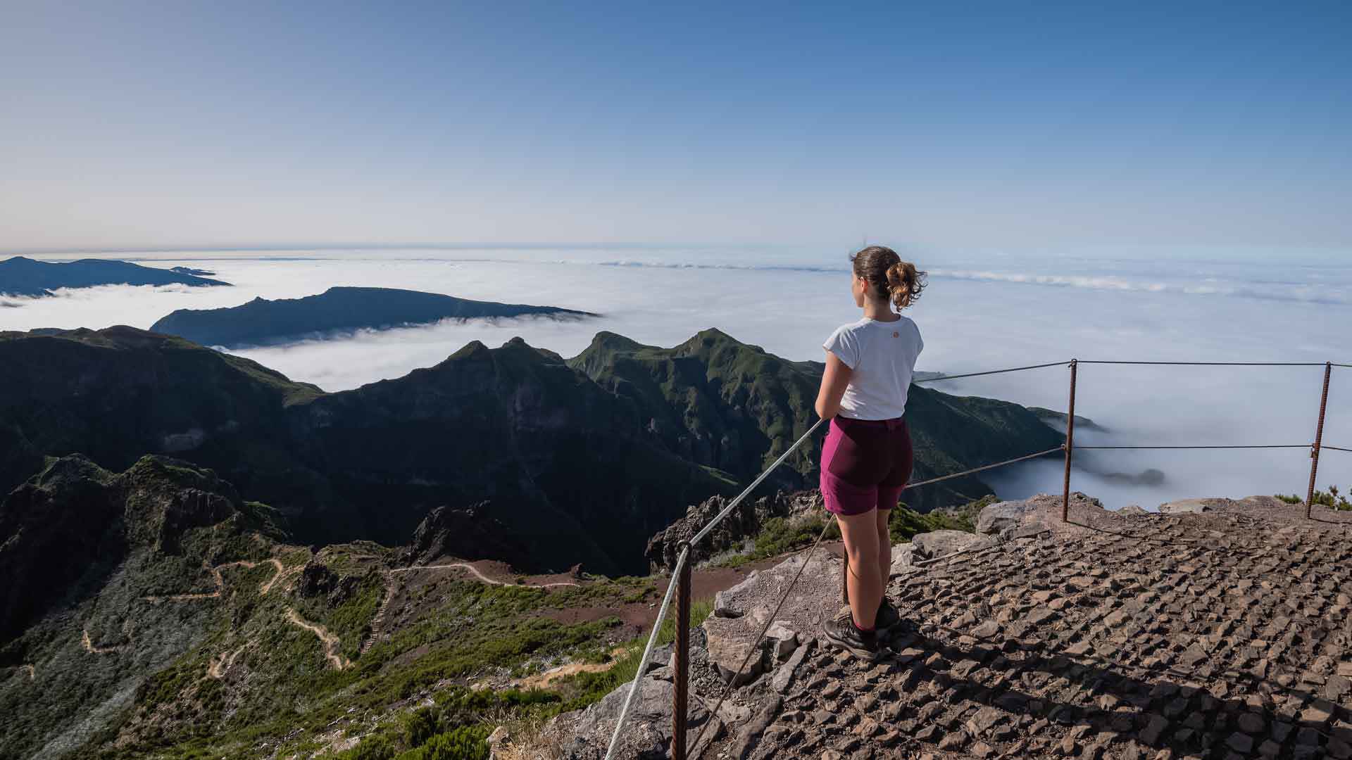 Woman at a viewpoint overlooking mountains and clouds in Madeira.
