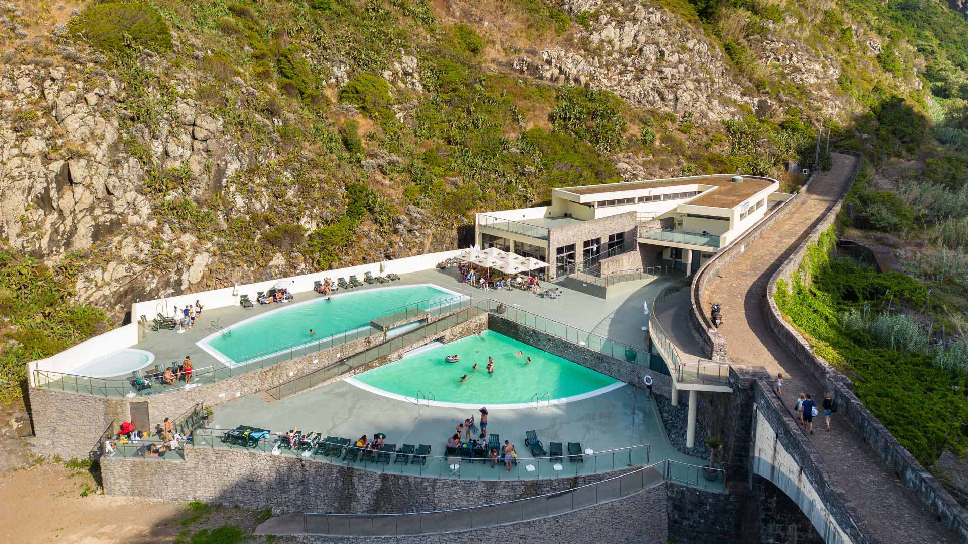 Personas en tumbonas junto a piscinas cerca de montañas de Madeira.