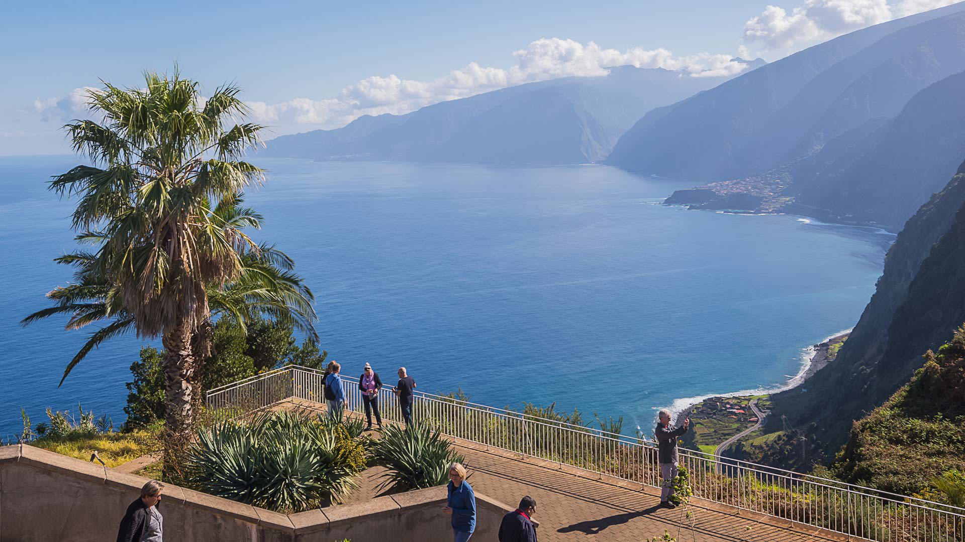 Aussichtspunkt mit Palme und Menschen, die die Küste und das Meer auf Madeira genießen.