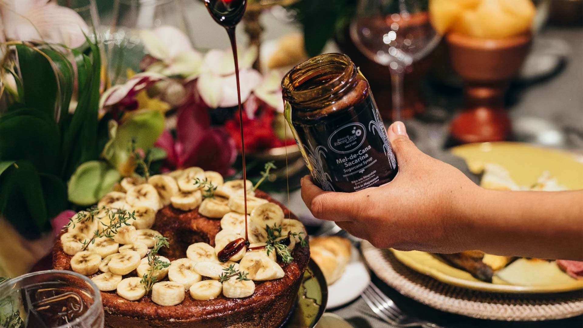 Hand drizzling sugarcane honey over a banana cake on a table at the Madeira Tourism Office in Lisbon.
