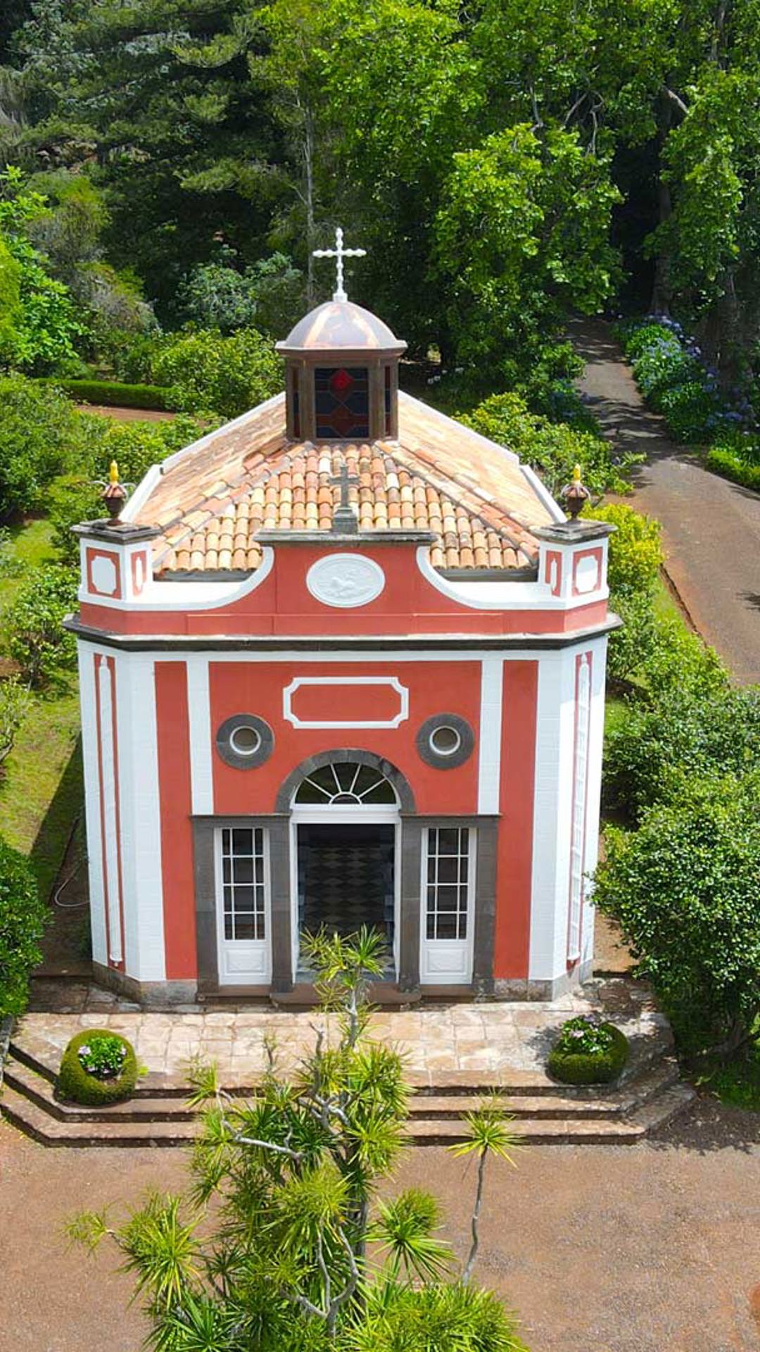 Igreja com fachada vermelha rodeada por vegetação.