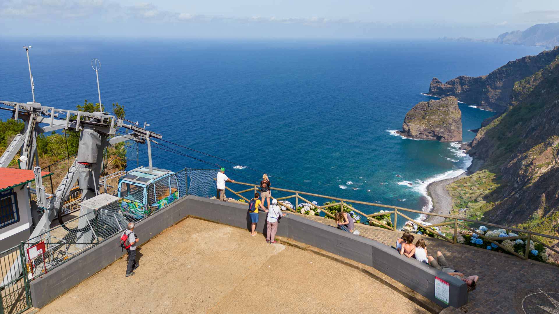 Teleférico com pessoas, mar e montanhas ao fundo na Madeira.