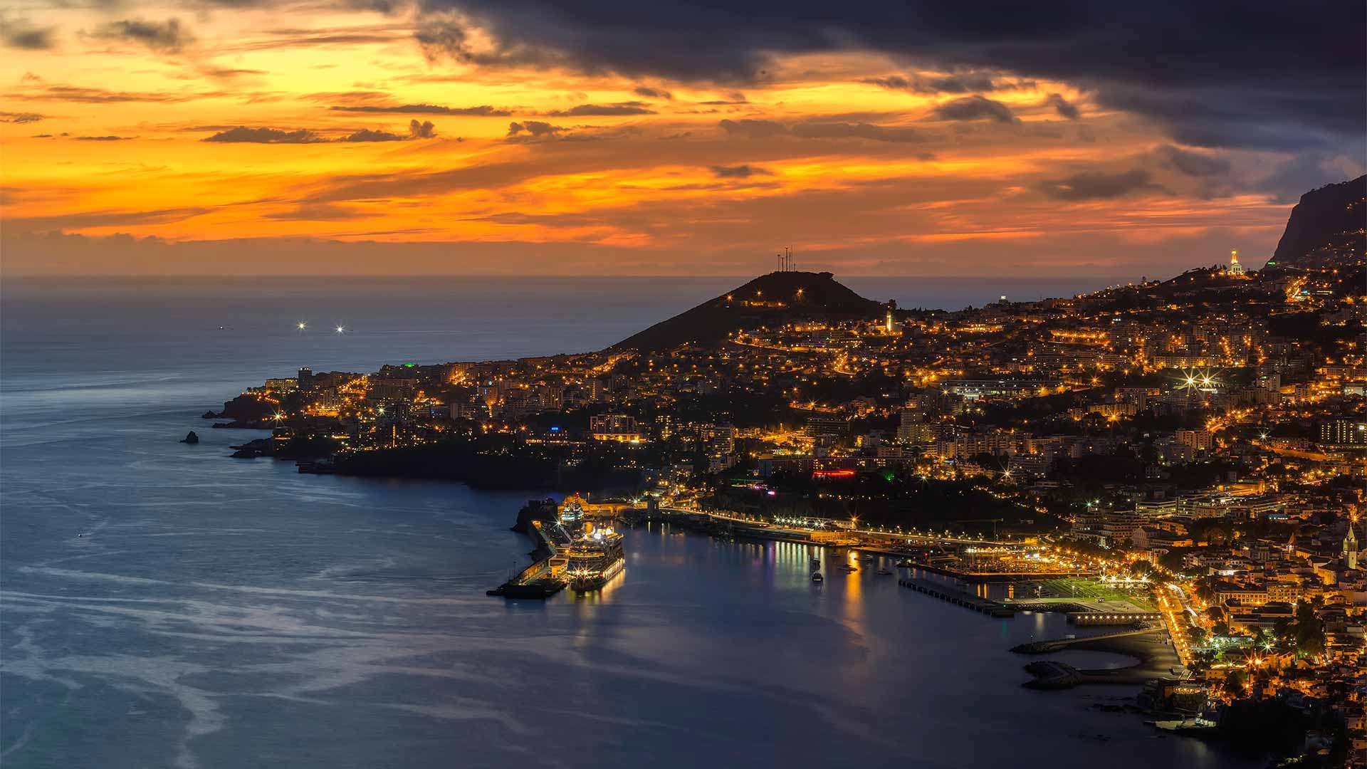 Sunset over the sea with coastal lights in Madeira.