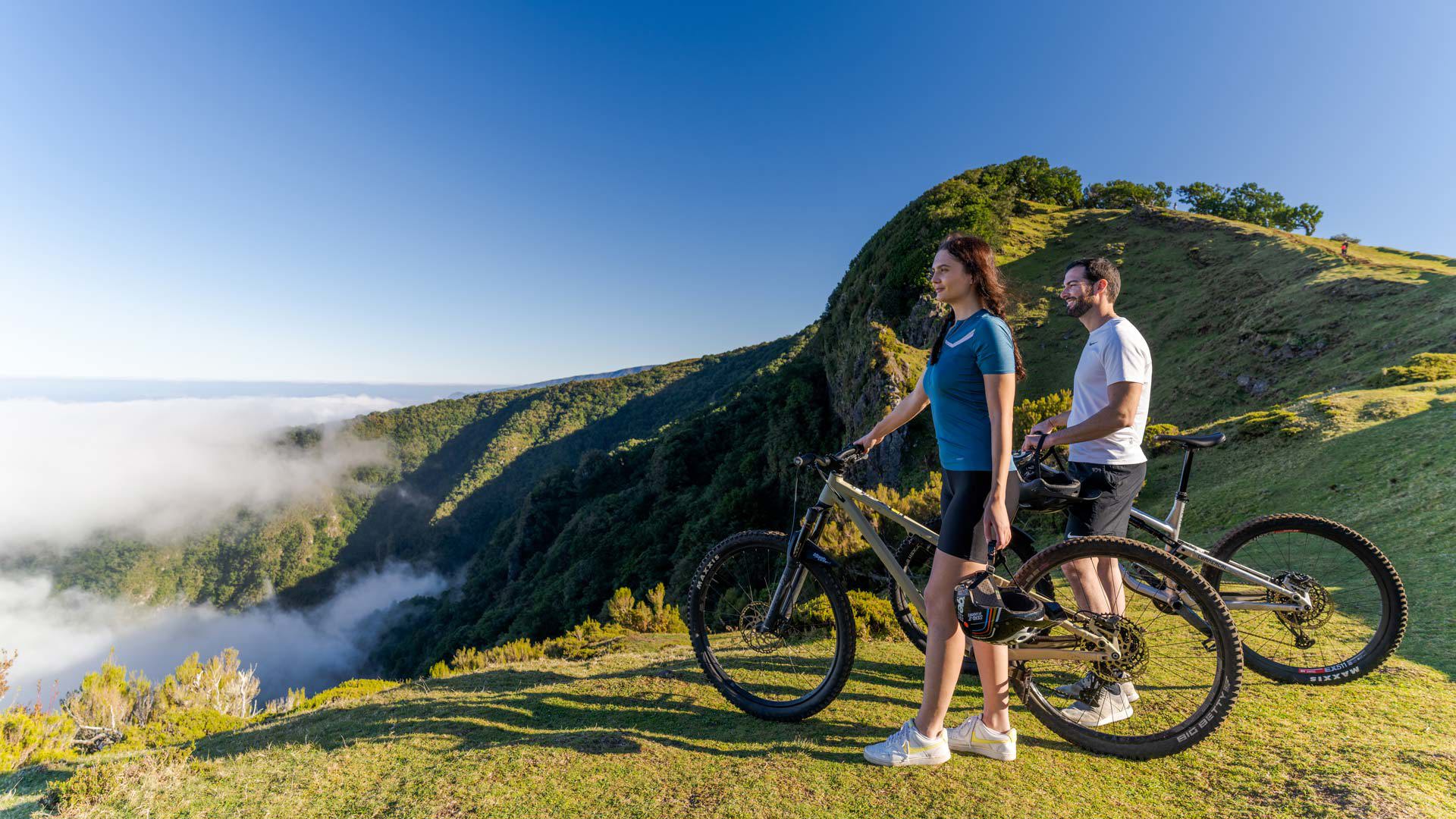Couple holding bicycles, admiring the view over nature above the clouds.